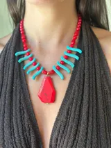 Collar de cuentas con dije central grande de piedra roja irregular, flanqueado por bastones turquesa y cuentas rojas redondas. La cadena es de eslabones finos con cierre regulable.