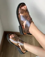 Sandalias marrones de cuero vacuno con tiras cruzadas y suela plana negra.