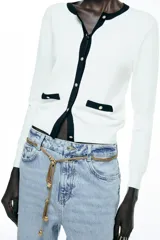 Chaqueta blanca de punto con cuello redondo y manga larga. Tiene falsos bolsillos de vivo en el delantero y cierre frontal con botones dorados.