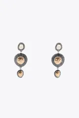 Aros colgantes metálicos plateados con tres dijes circulares con textura y apliques de joya, abalorios y piezas labradas combinadas a contraste. Cierre con tuerca.