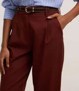 Pantalón zanahoria de cintura alta color borgoña, con trabillas, pliegues y cinturón fino de cuero sintético.