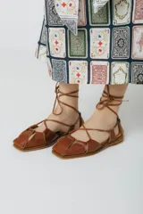 Sandalias chatitas de cuero color bordó, con puntera cuadrada y tiras finas que se atan al tobillo.