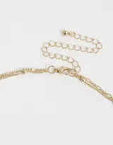 Collar corto dorado con doble cadena, una con eslabones y otra con perlas colgantes. Dije de corazón con strass incrustado.