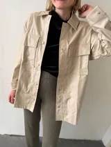Sobrecamisa negra de ecocuero con cuello clásico, cierre frontal con botones a presión, mangas largas con puños abotonados, dos bolsillos de parche con solapa en el pecho y corte recto.