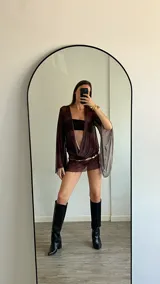 Vestido corto marrón traslúcido con escote en V profundo, mangas largas acampanadas y cinturón dorado.