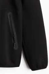 Campera deportiva negra con capucha, cierre frontal, bolsillos con cierre y mangas raglán. Confeccionada en tejido funcional efecto neopreno DryMove™ que ayuda a absorber el sudor.