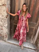 Vestido largo de seda con estampado tie-dye en tonos rojo y blanco, con mangas cortas con volados y ruedo con volados.