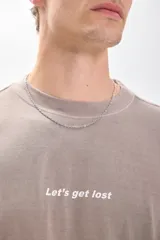 Camiseta manga corta color beige con estampa en la espalda que dice "DON'T STOP UNTIL YOU ARE UNSTOPPABLE", "Let's get lost", "BASED IN SOUTH AMERICA LIVE THE MOMENT Contemporary 1995". Corte amplio y recto, más ancha que larga y sin ajuste al cuerpo.