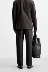Pantalón de vestir negro de corte recto, confeccionado en tejido de algodón con acabado ligeramente encerado. Cuenta con bolsillos laterales y traseros de vivo. El cierre frontal es con cremallera y gancho metálico oculto.