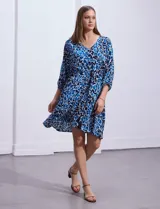 Vestido corto de rayón con estampado floral en tonos azules y blancos. Tiene escote en V, mangas 3/4 con puño, cintura con lazo de ajuste y borlas.