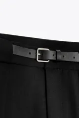 Pantalón negro de tiro medio con cinturón a tono con hebilla metálica, bolsillos delanteros y falsos bolsillos traseros.