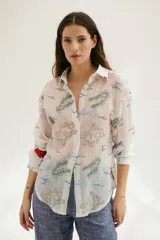Camisa beige de manga larga con cuello clásico y cierre frontal con botones. Presenta bordados con motivos florales y geométricos en tonos azules, rojos y verdes.