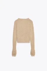 Chaqueta de punto color beige con cuello redondo y mangas largas terminadas en flecos. Cierre frontal con ganchos ocultos.