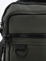 Bandolera color verde militar con correa larga regulable negra, bolsillo frontal con cierre y asa de mano superior.