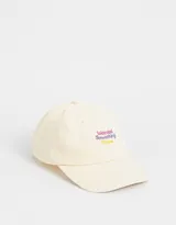 Gorra de béisbol color crema, de tela canvas, con visera curva y bordado frontal con la frase "Wanted Something More" en letras color lila y amarillo.
