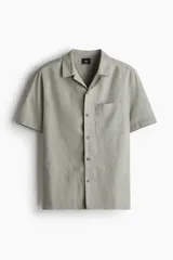 Camisa de manga corta color verde oliva, con cuello cubano, bolsillo de parche en el pecho y cierre frontal con botones. Corte regular fit.