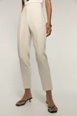 Pantalón de vestir color crema, de tiro alto, corte recto y largo cropped. Presenta bolsillos laterales de ojal y cierre frontal con cremallera, botón interior y gancho metálico.