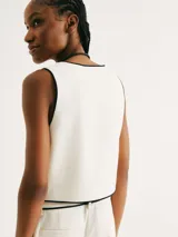 Chaleco blanco con ribete negro, cuello en V y cierre frontal con botones.