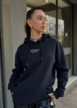 Hoodie negro de corte holgado con capucha y cordón ajustable. Estampado frontal con la leyenda "BE TRENDY EST. 2022" en color rosa.