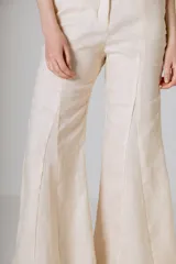 Pantalón de lino color beige, corte flare, tiro medio y costuras verticales al frente.