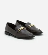 Zapato mocasín de cuero color marrón oscuro con detalle metálico dorado en la parte delantera.