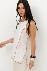 Musculosa color crudo con cuello redondo y ribete marrón en cuello, sisas y ruedo. Diseño cruzado en el frente y aberturas laterales.