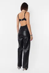 Pantalón negro de cuerina, de corte recto, tiro medio-bajo, con bolsillos delanteros y traseros, presillas en la cintura y cierre metálico.