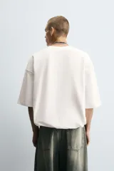 Camiseta blanca de algodón, corte holgado, cuello redondo, manga corta y bajo con elástico interior.