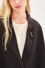 Saco de lino color negro, de corte amplio, con solapa, bolsillos falsos y pin de guitarra en la solapa.