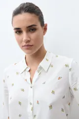 Camisa blanca de manga larga con cuello abotonado y estampado de pequeñas flores en tonos naranjas y verdes.