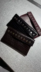 Billetera de ecocuero con textura símil cocodrilo, cierre con botón a presión, tres compartimentos para billetes, seis compartimentos para tarjetas (con capacidad para 12 tarjetas) y sobre de regalo para monedas.