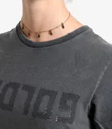 Remera gris de algodón con cuello redondo y calce entallado. Presenta un efecto desgastado y un estampado con la palabra 'GOLD' en el frente.