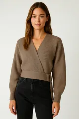 Sweater de punto acanalado color marrón, con diseño cruzado tipo wrap, escote en V y detalle de hebilla lateral en la cintura. Presenta mangas largas con puños ajustados.