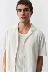 Camisa de manga corta color crema, de punto texturizado de mezcla de algodón de peso medio. Modelo con cuello abierto, tapeta lisa y bajo recto.