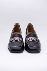 Zapato de cuero negro con aplique plateado y botones forrados en cuero.