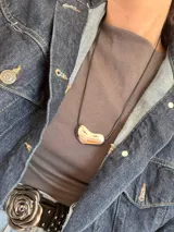 Collar con cadena fina negra y dije plateado con forma irregular.