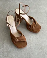 Sandalia de cuero vacuno color dorado, con plataforma y taco cuadrado. Presenta una tira delgada en el tobillo y detalle de nudo en la capellada.