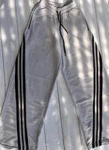 Pantalón de jogging color gris claro con cordón ajustable en la cintura y tres rayas verticales negras a los costados.