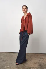 Blusa color ladrillo confeccionada en lino 100%. Tiene cuello fluido, mangas largas acampanadas y espalda descubierta ajustable con cordones.