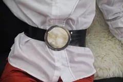 Cinturón con hebilla circular de guampa y engarce en alpaca, con tira de cuero rojo.