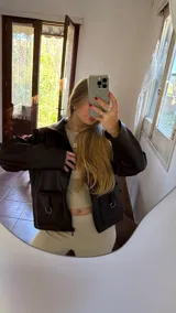 Campera corta de ecocuero marrón oscuro con cierre frontal y dos bolsillos con argollas decorativas.