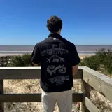 Camisa de lino negra con estampado de figuras geométricas en color gris claro en la espalda. Corte boxy, cuello clásico y mangas cortas.