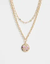 Collar corto dorado con doble cadena, una de eslabones grandes y otra de eslabones pequeños. Dije redondo con diseño de moño rosa y strass.