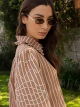 Camisa de denim azul con cuello camisero con volados, mangas largas abullonadas con puños elastizados y bordado blanco en las mangas.