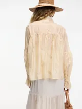 Camisa color crema bordada con botones en la parte delantera, mangas largas con media manga abullonada y cuello camisero.