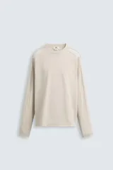 Camiseta color beige de corte relaxed fit, con cuello redondo y mangas largas combinadas con tejido de red.
