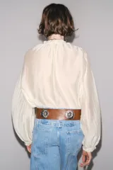 Camisa color crema de algodón con cuello redondo, escote pico con lazadas, manga larga con puños y cierre frontal con botones.