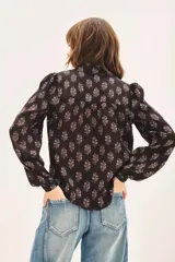 Camisa negra con estampado floral blanco, de corte regular, con volados en el cuello y cierre frontal con botones.