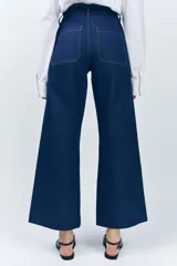 Pantalón de jean de tiro alto color negro con pierna ancha, bolsillos delanteros y traseros, y cierre frontal con cremallera y botón metálico.
