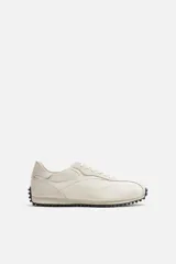 Zapatillas deportivas color crema con cordones, estilo retro. Parte superior fabricada en tejido técnico y detalles en piel con acabado serraje. Suela dentada con detalle a contraste en negro.